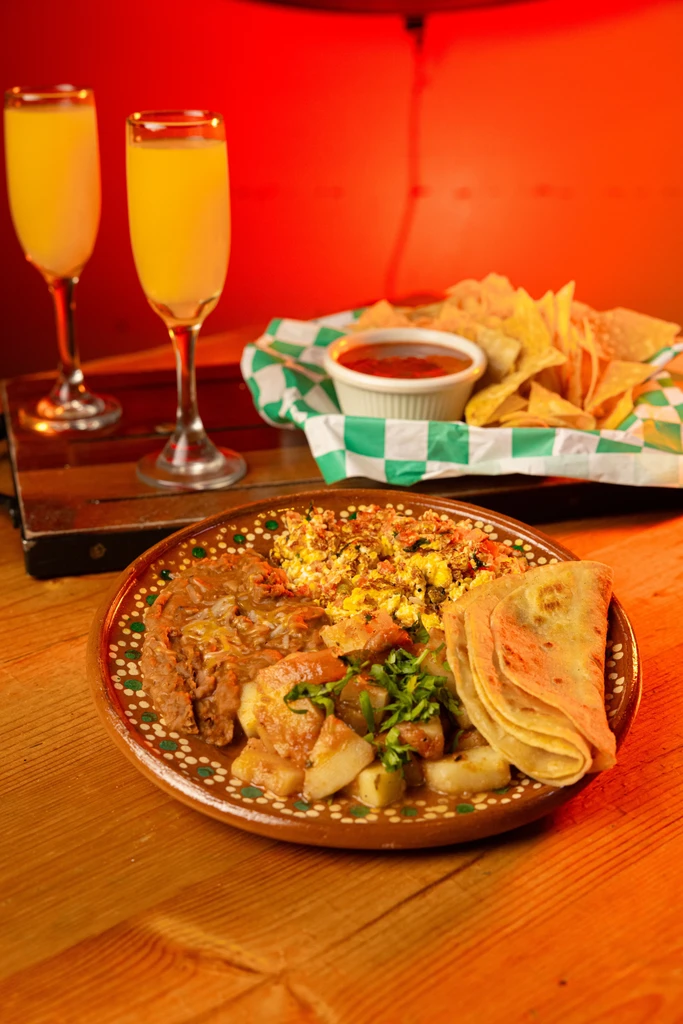 Large plate of Mexican breakfast food with chips, salsa, and mimosas.