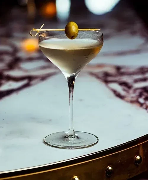 Chilled martini glass with olive on marble, metallic edge.