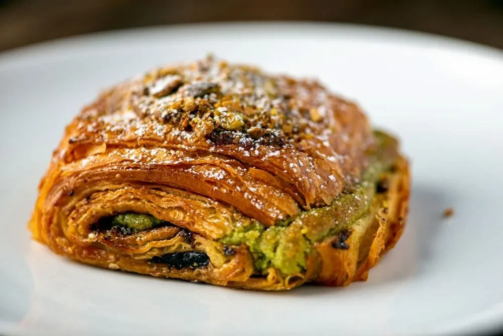 Flaky pastry with green filling, powdered sugar, and nuts.