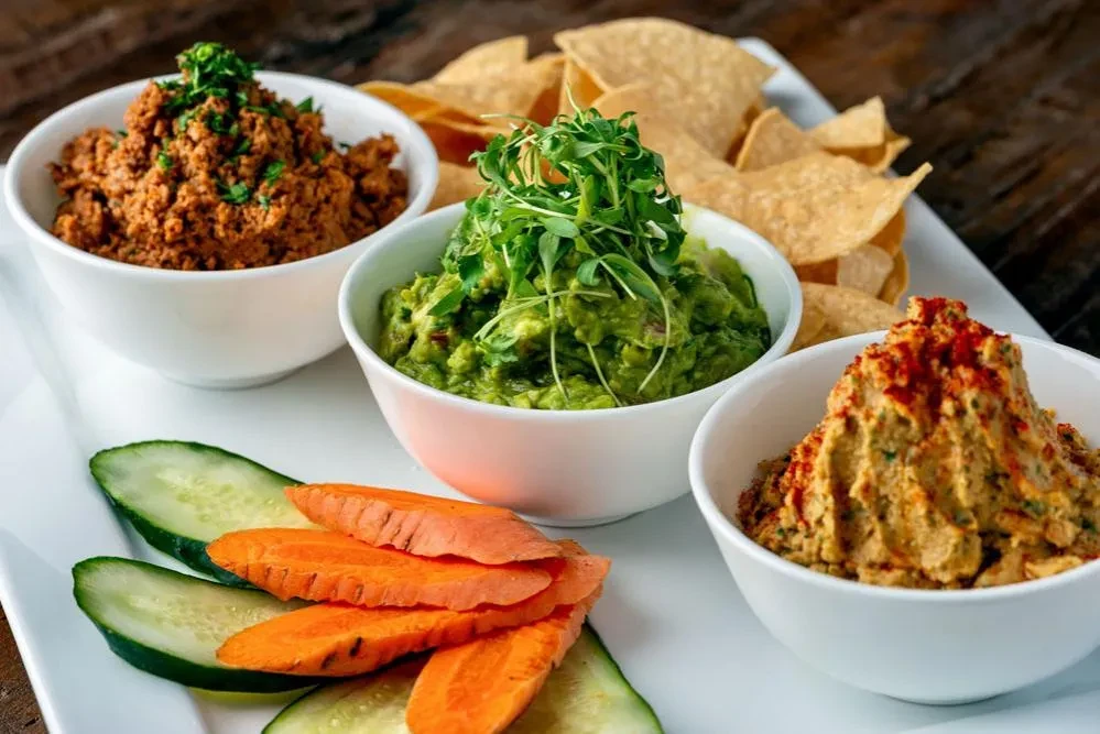 Platter of red, green, tan dips with vegetables and tortilla chips.