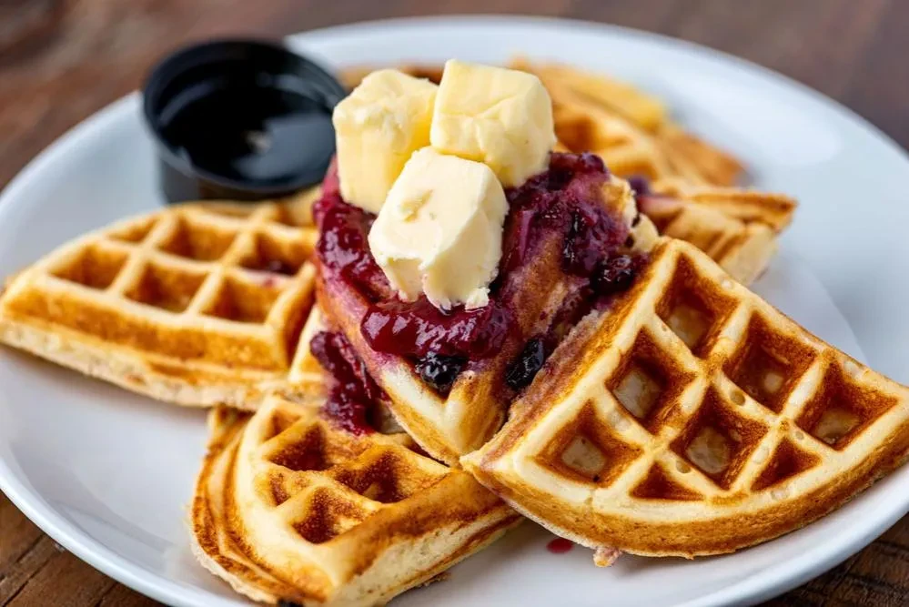 Golden-brown waffles with dark berry compote and melting butter.