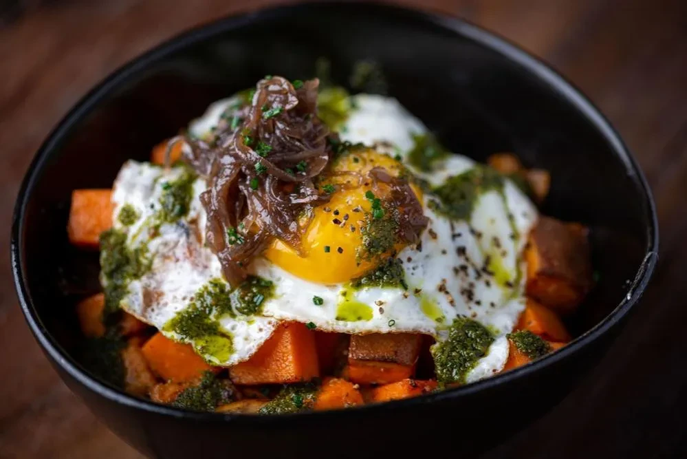 Two fried eggs on sweet potatoes with caramelized onions and green pesto.