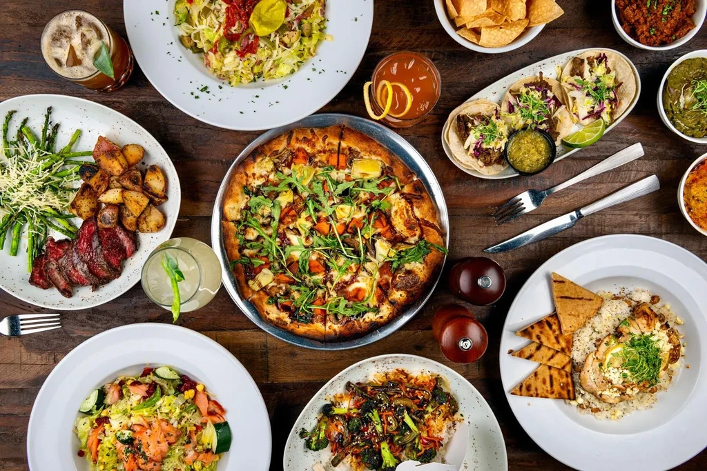 Overhead flat lay of diverse dishes and drinks on a wooden table.