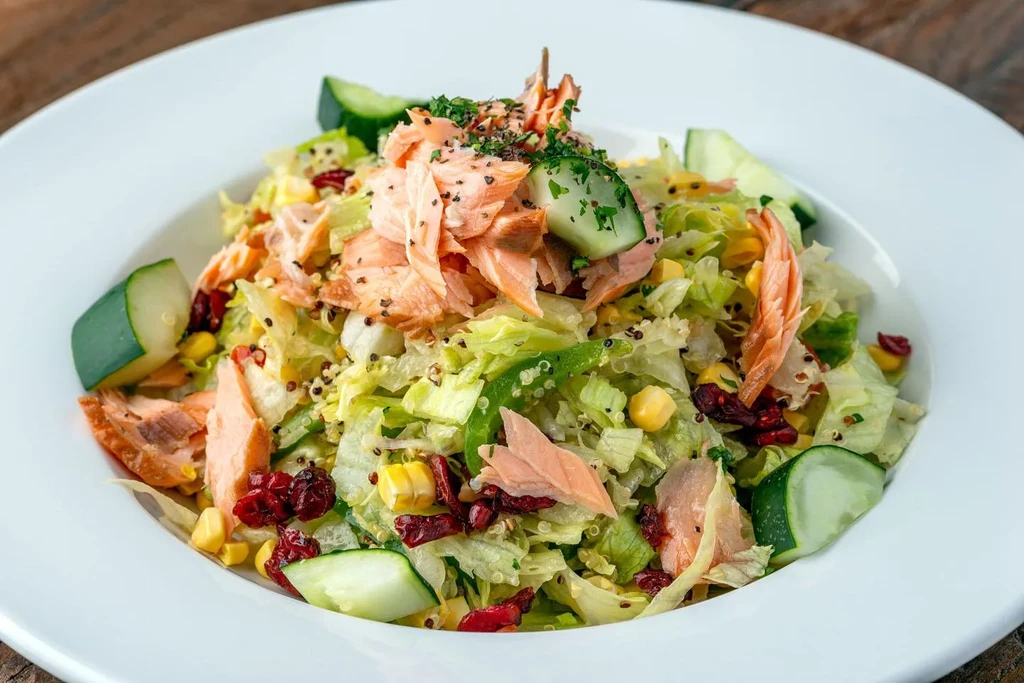 Close-up vibrant salmon salad with lettuce, corn, cucumber, cranberries, and quinoa.