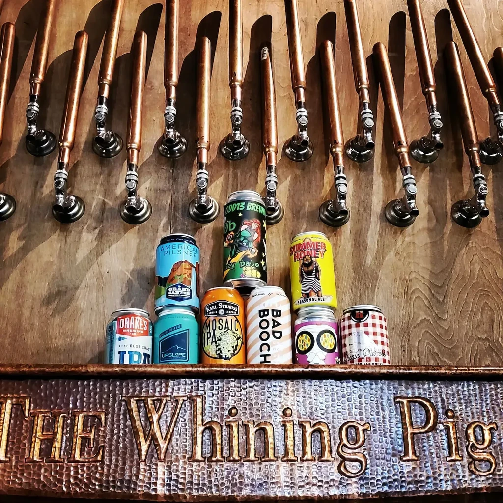 Diverse craft beer cans, copper taps, and "THE Whining Pig" sign.
