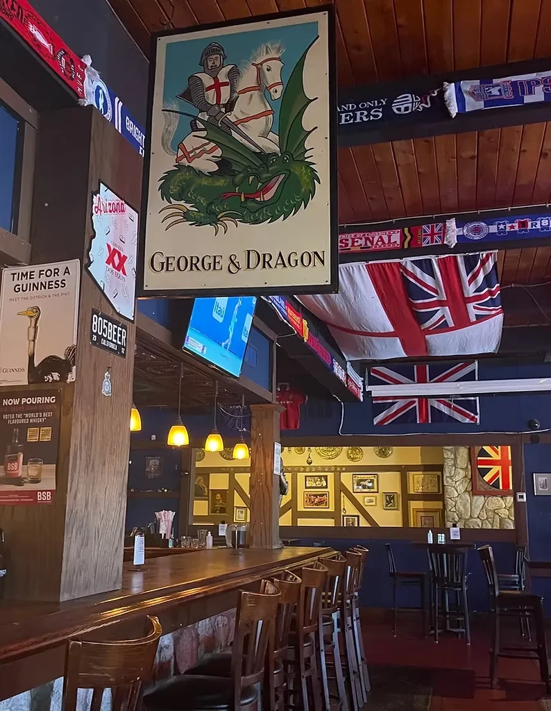 British pub interior: wooden bar, St. George sign, Union Jacks, football scarves.