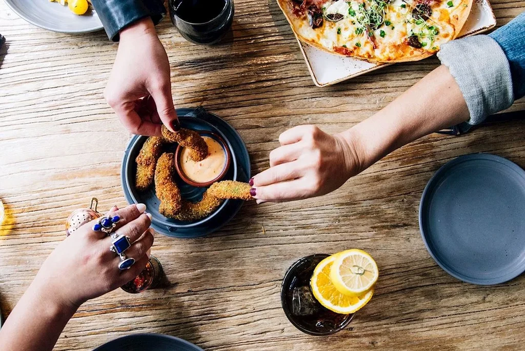 Overhead view of hands sharing fried food and flatbread on a table.