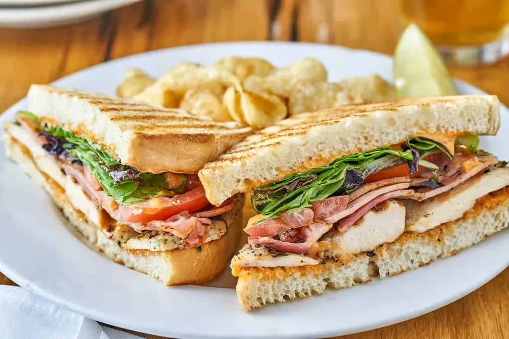 Grilled chicken panini with lettuce, tomato, chips, and lime on a plate.