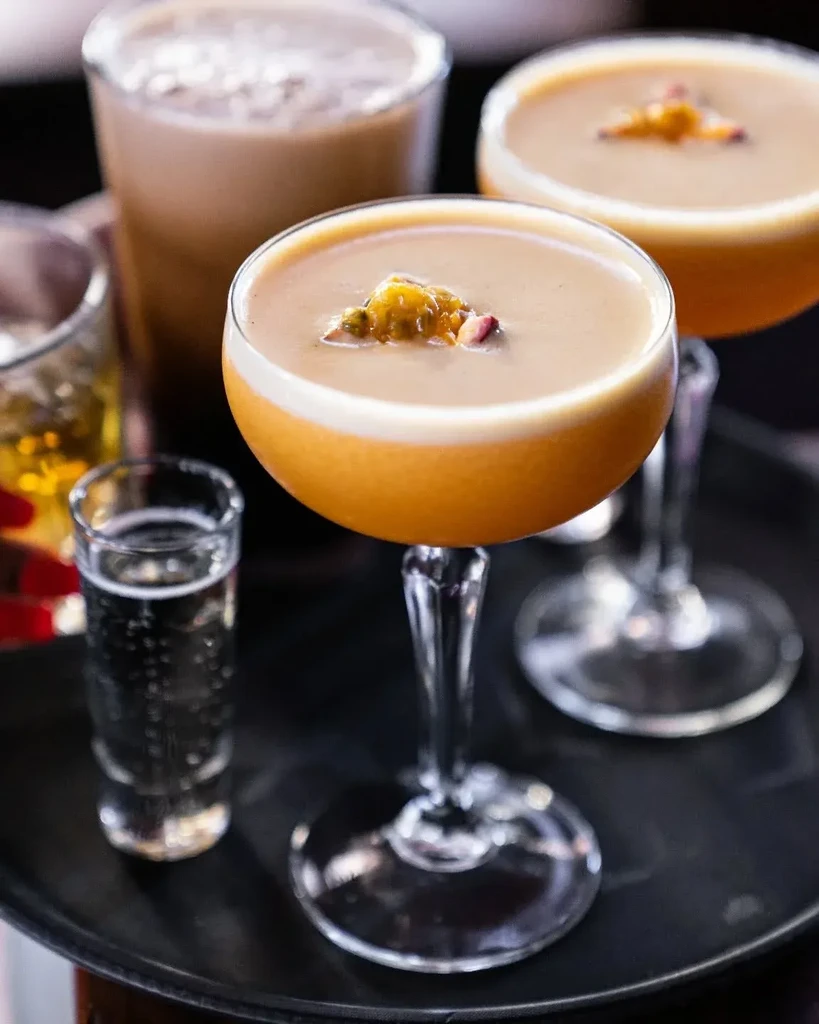 Orange frothy cocktail with passion fruit and other drinks on a tray.
