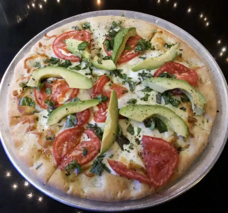 White sauce pizza with tomatoes, avocado, and herbs on a metal pan.