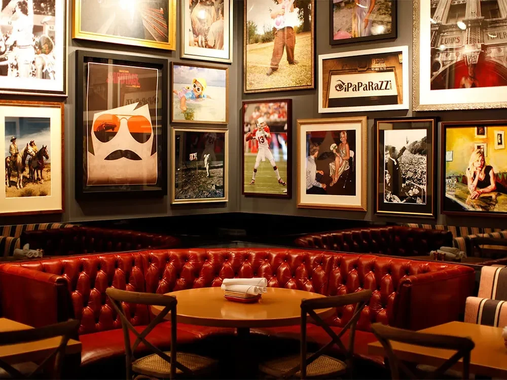 Empty restaurant interior with red leather banquettes and framed art.