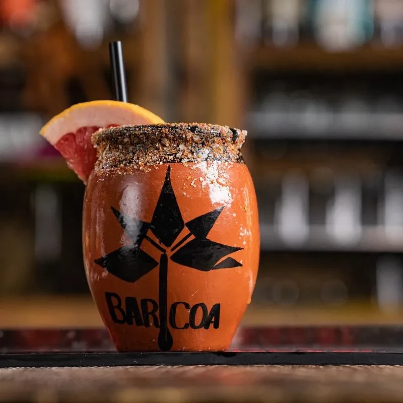 Cocktail in rust-orange 'BAR COA' mug with spiced rim and grapefruit.