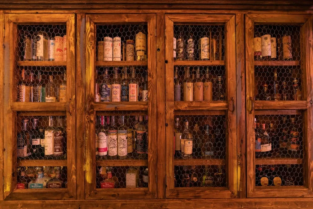 Rustic wooden cabinet with chicken wire panels filled with liquor bottles.