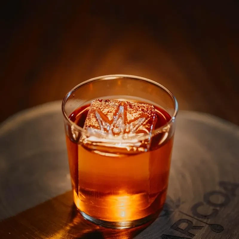 Amber cocktail in old-fashioned glass with cannabis leaf ice cube.