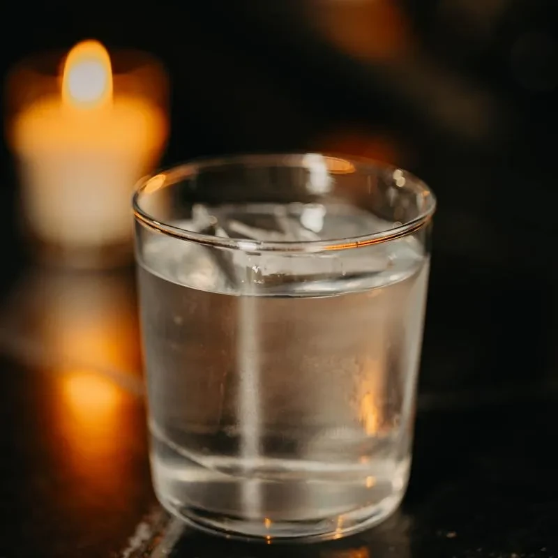Glass of water and ice with condensation, blurred candle glow.