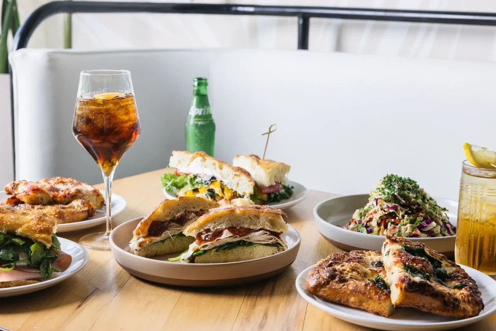 Well-lit spread of sandwiches, salad, and drinks on a restaurant table.