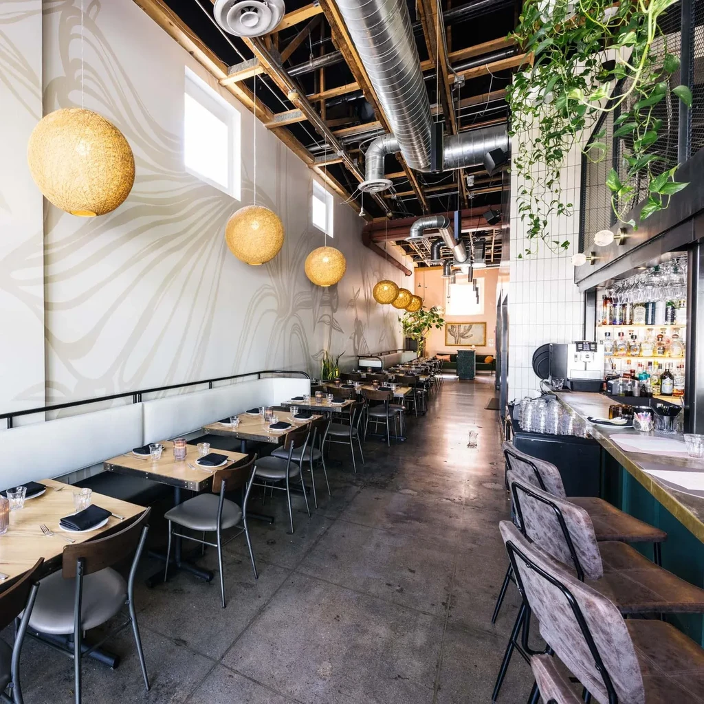 Empty, modern restaurant interior with dining area, bar, and industrial-chic decor.