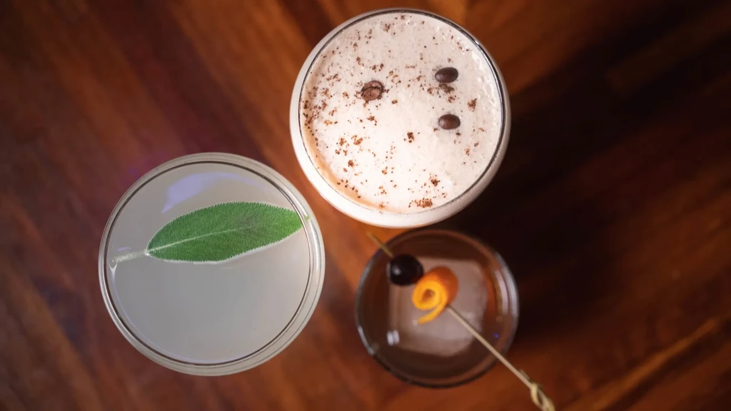 Espresso, sage-garnished, and whiskey cocktails on a wooden surface.