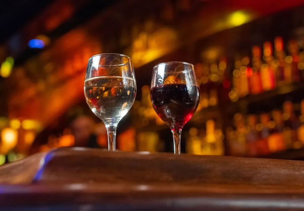 Two wine glasses, one white and one red, on a wooden bar.