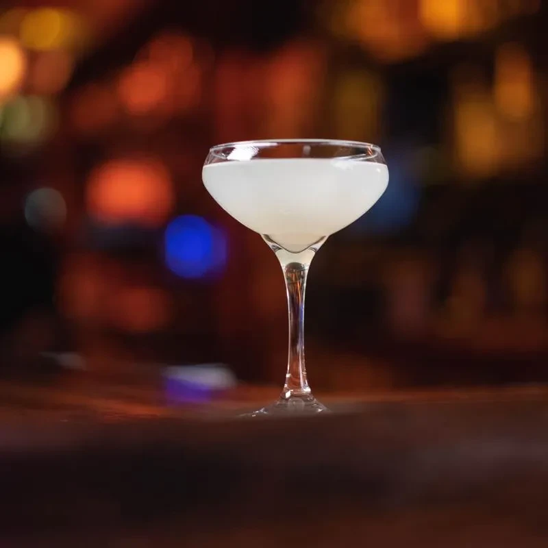 Opaque white cocktail in a coupe glass, blurred bar background.