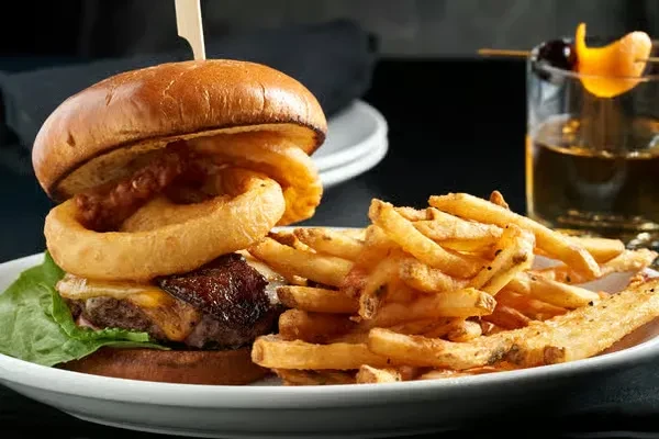 Gourmet burger with onion rings, fries, and amber cocktail.