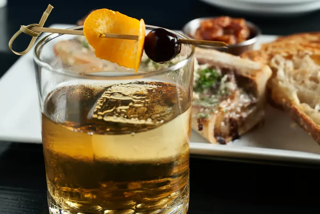 Close-up: Amber drink in rocks glass with ice, orange, cherry.