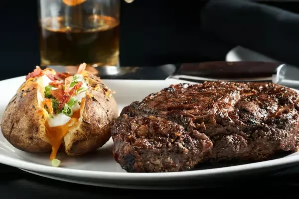 Seared steak, loaded baked potato, and amber drink on a plate.