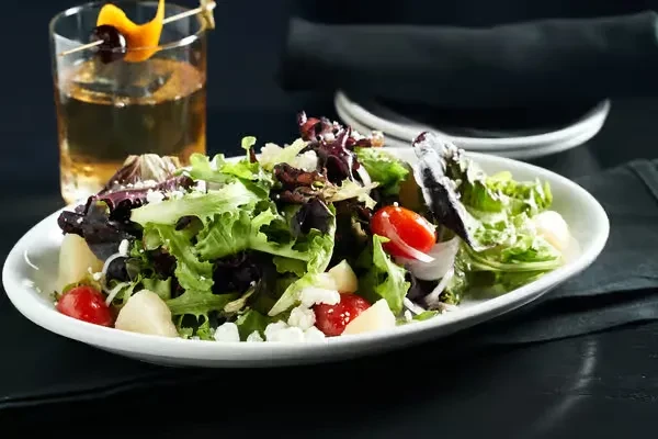 Vibrant mixed green salad and amber cocktail on a dark table.