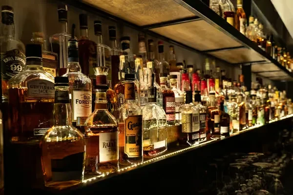 Neatly arranged, illuminated bar shelf stocked with whiskies and bourbons.
