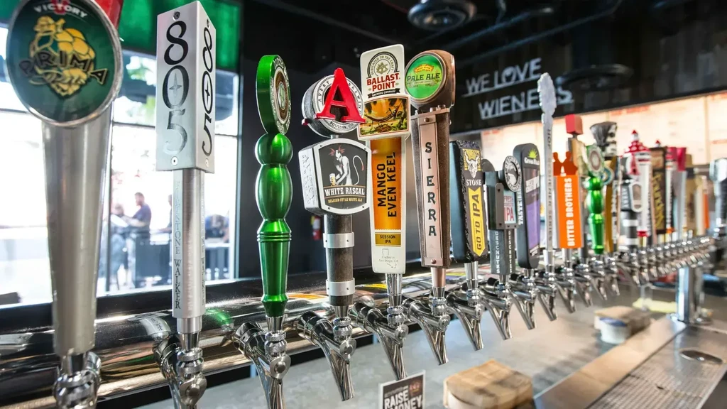 Numerous branded draft beer taps with a 'WE LOVE WIENERS' sign above.