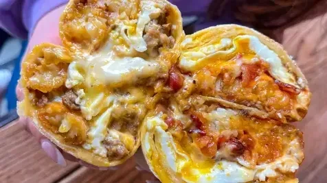 Halved breakfast burrito revealing eggs, melted cheese, and ground meat filling.