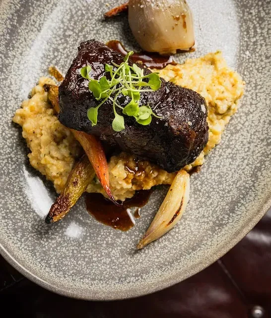 Dark glazed meat on creamy grains with roasted vegetables.