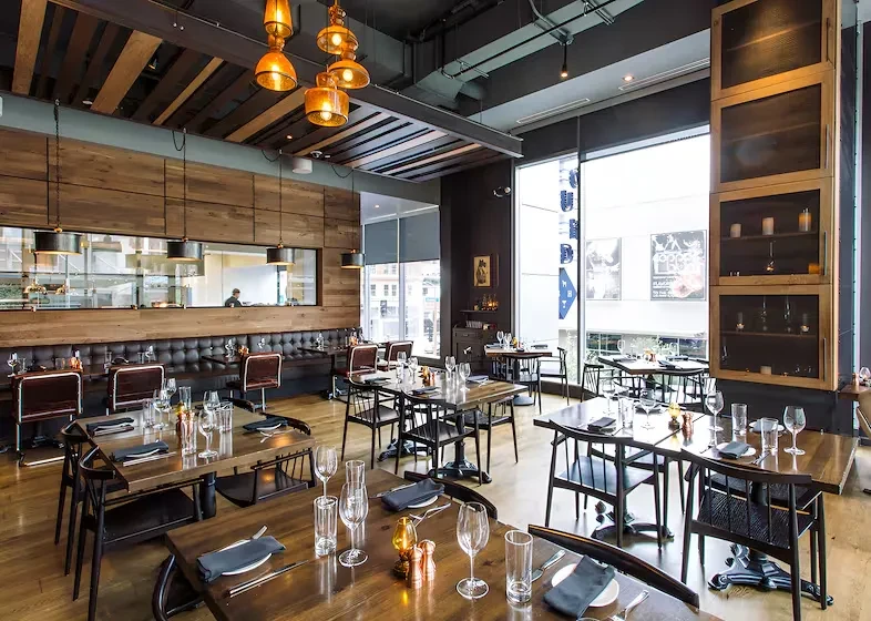Restaurant with amber lights, wood panels, tufted banquette, and industrial ceiling.