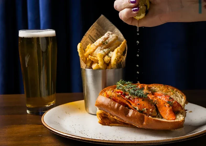 Lobster roll, waffle fries, beer, and hand squeezing lemon.