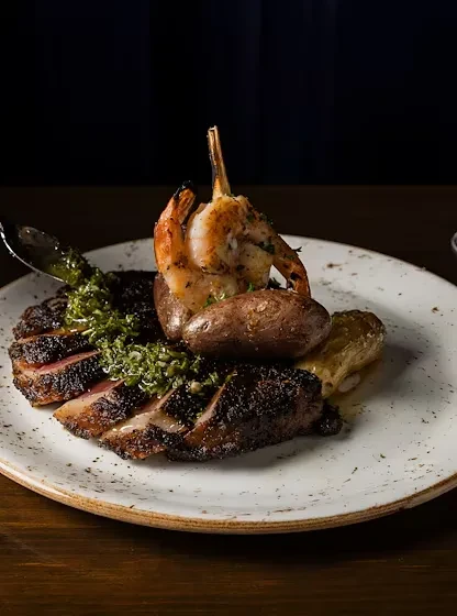 Sliced medium-rare steak, green sauce, roasted potatoes, grilled shrimp.