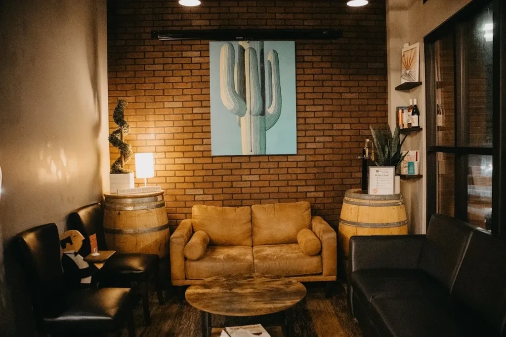 Warmly lit lounge with saguaro painting, leather sofa, and wine barrels.