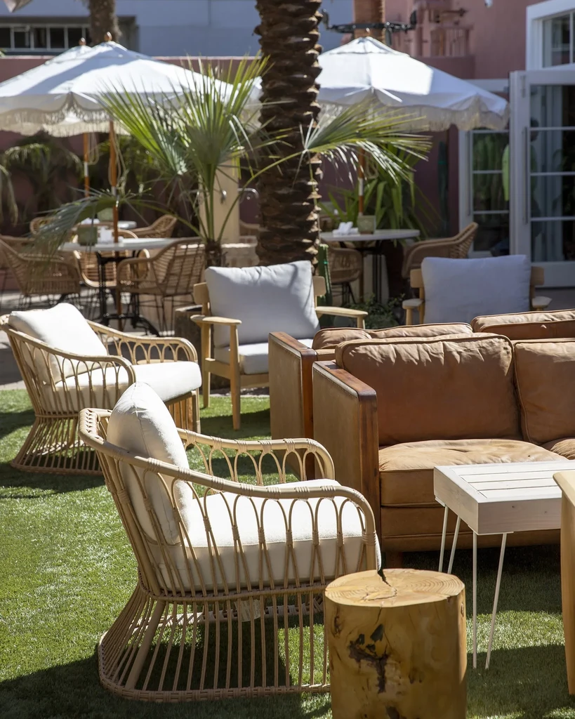 Green turf patio with wicker chairs, sofa, palm trees, and umbrellas.