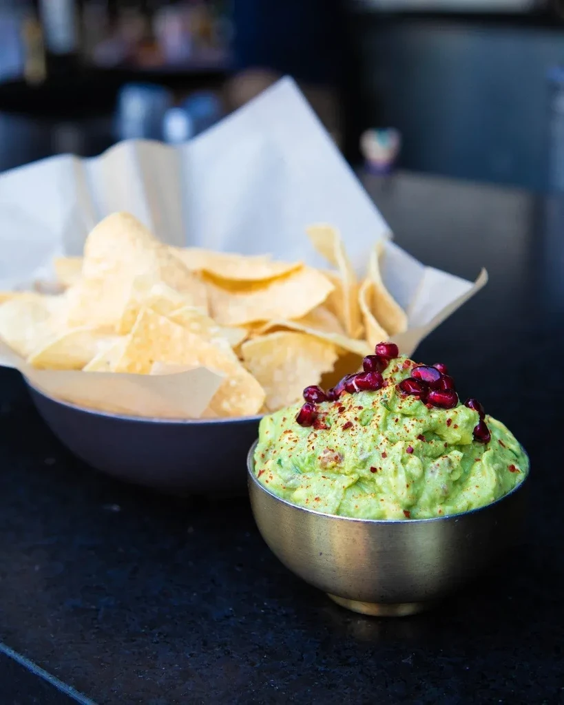 Guacamole with pomegranate seeds and tortilla chips on dark counter.