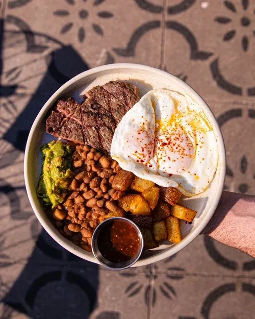 Overhead: Bowl of grilled meat, eggs, beans, guacamole, potatoes, and sauce.