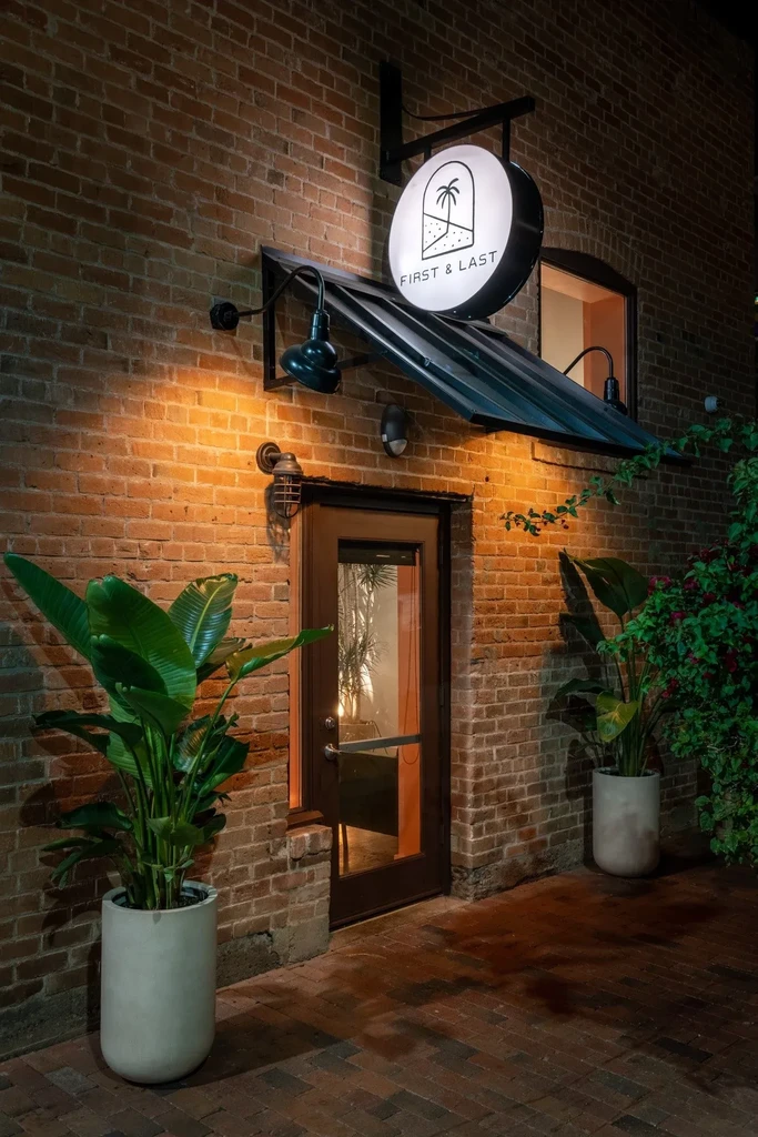 Illuminated brick restaurant entrance with "FIRST & LAST" sign.