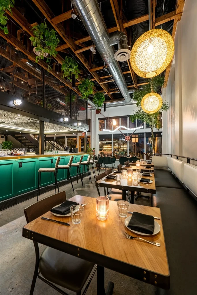 Industrial-chic restaurant interior with teal bar, wooden tables, and plants.