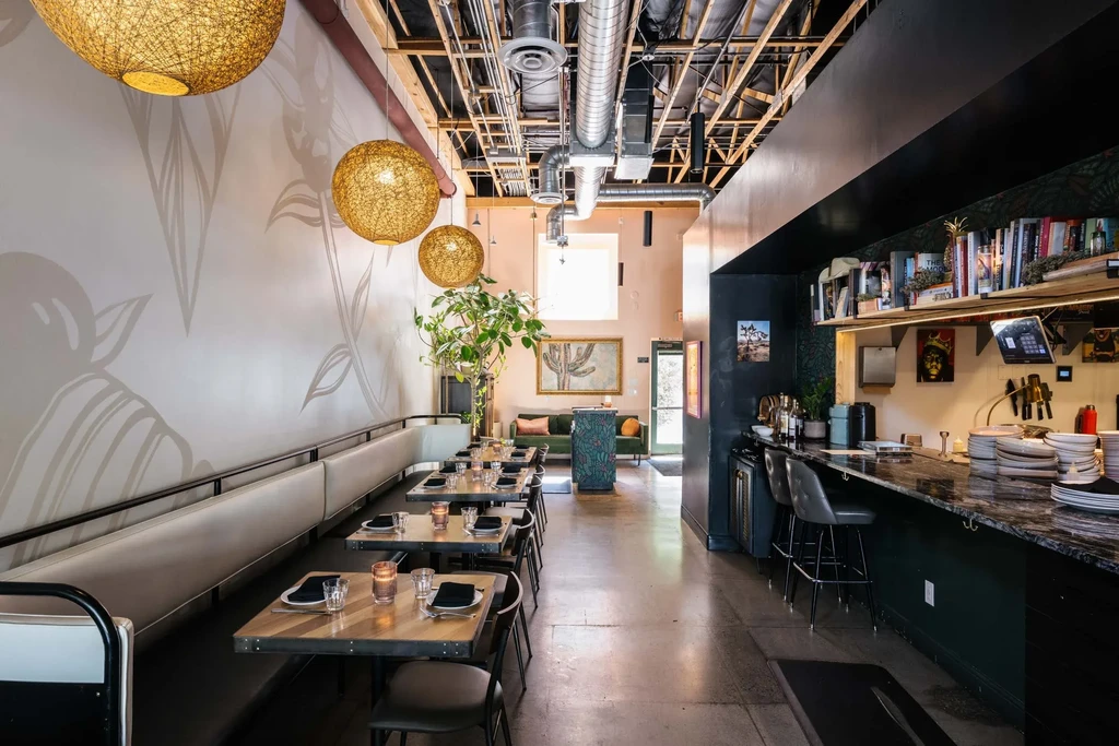 Modern restaurant interior with banquette, industrial ceiling, dark bar, and lounge.
