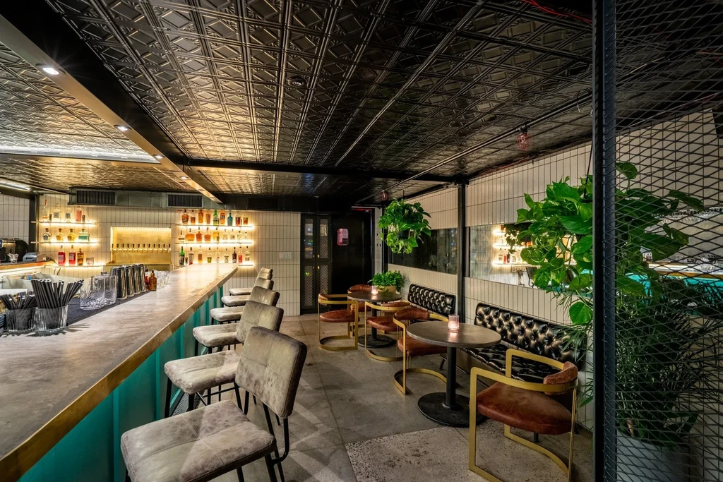 Empty modern bar with teal counter, illuminated liquor, and diverse seating.