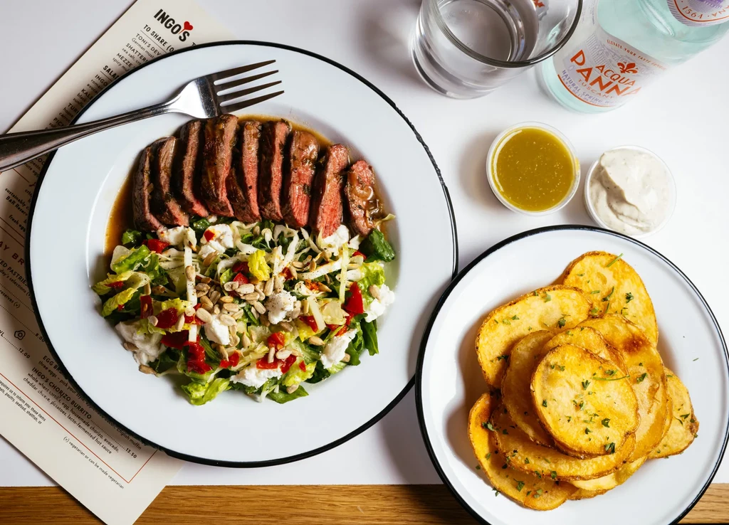 Overhead shot: Steak salad, potato chips, water, sauces, and INGO'S menu.