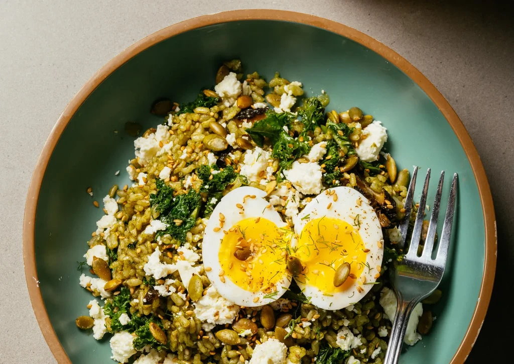 Teal bowl with grain, greens, feta, seeds, and soft-boiled eggs.