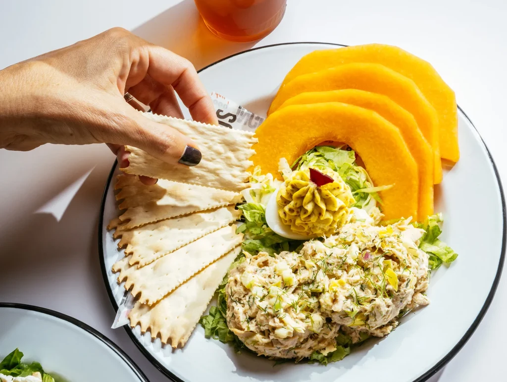 Overhead: Hand picks cracker from tuna salad, deviled egg platter.