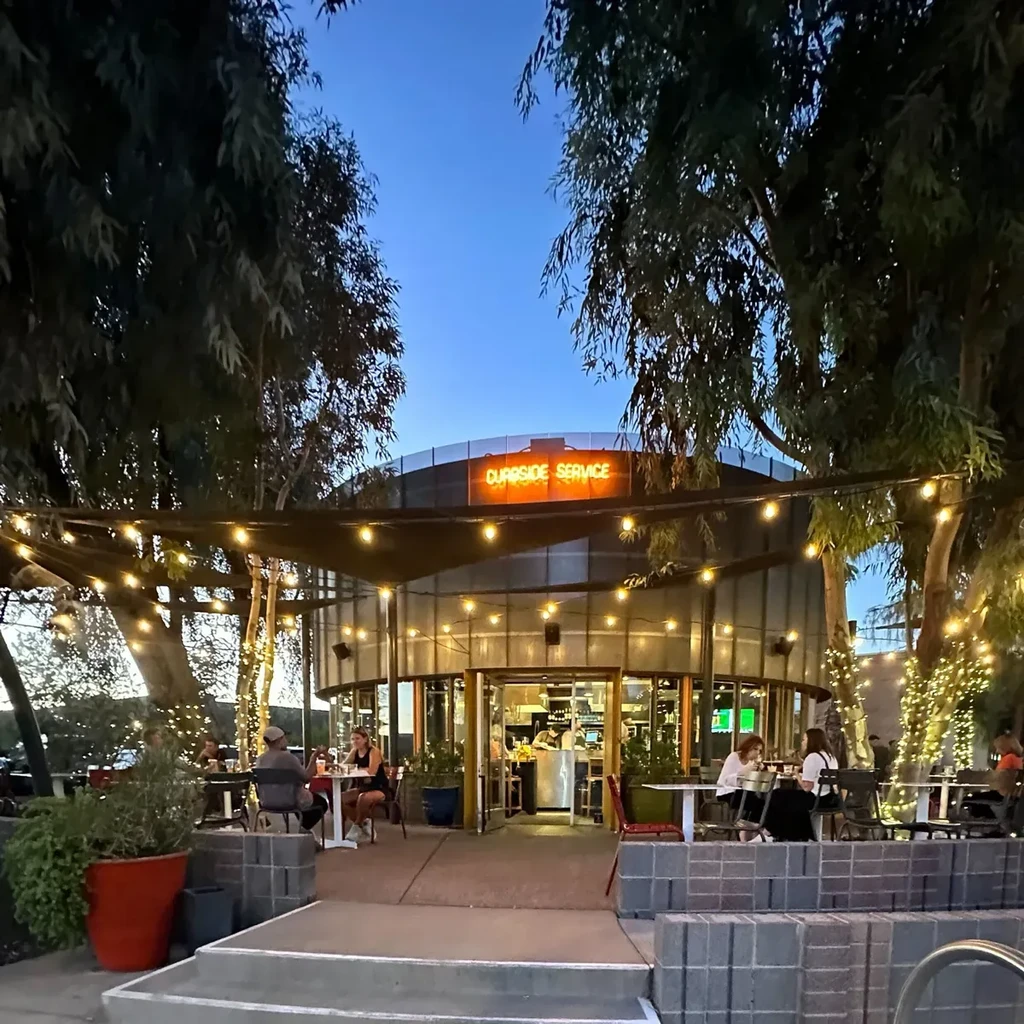 Illuminated outdoor dining patio with diners and a "Curbside Service" sign.