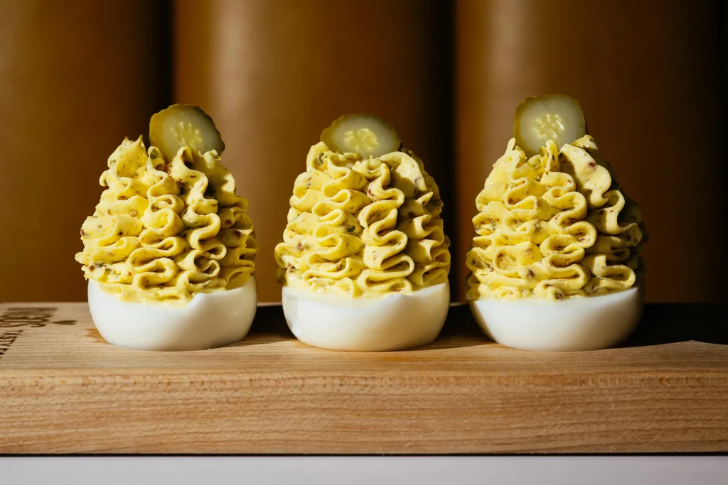 Three deviled eggs with piped yolk and pickle on wooden board.