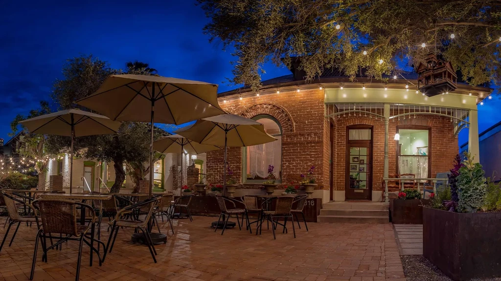 Empty restaurant patio at dusk with tables, umbrellas, and string lights.