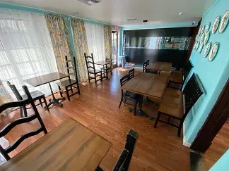 Empty restaurant dining area with wooden tables, turquoise walls, floral curtains.